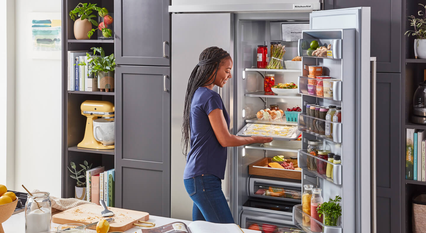 A woman in her kitchen, standing in front of a KitchenAid® built-in refrigerator