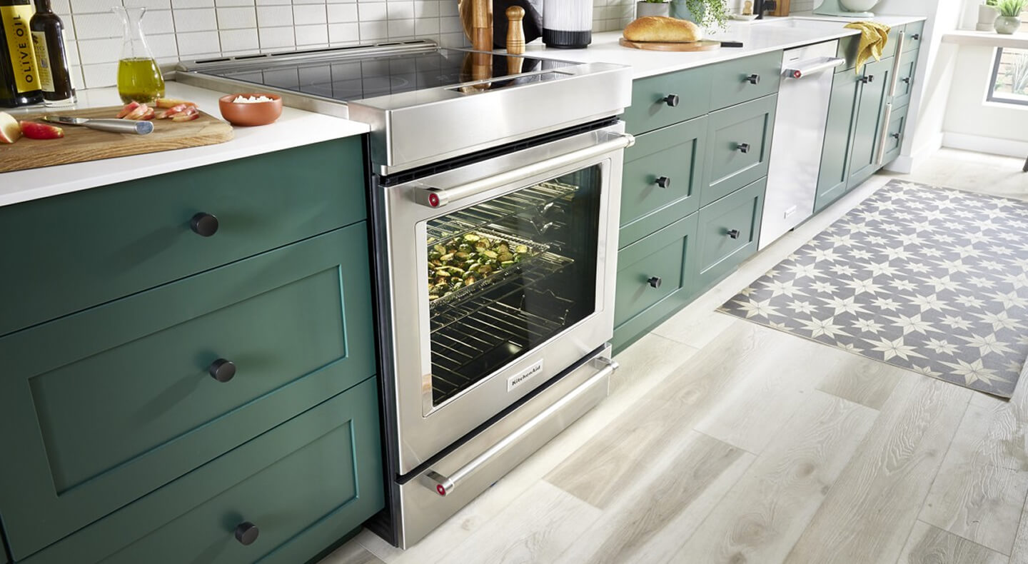 Electric slide-in range surrounded by dark green cabinetry