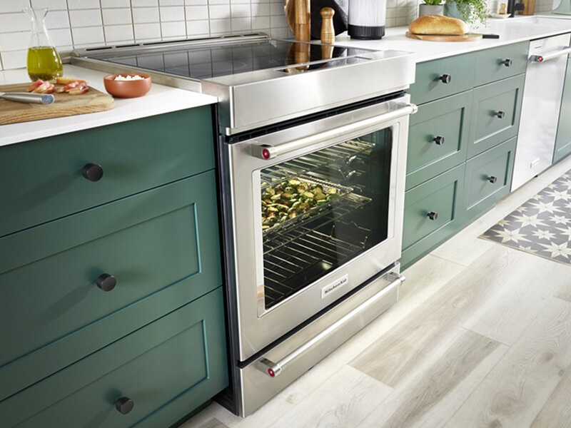 Electric slide-in range surrounded by dark green cabinetry