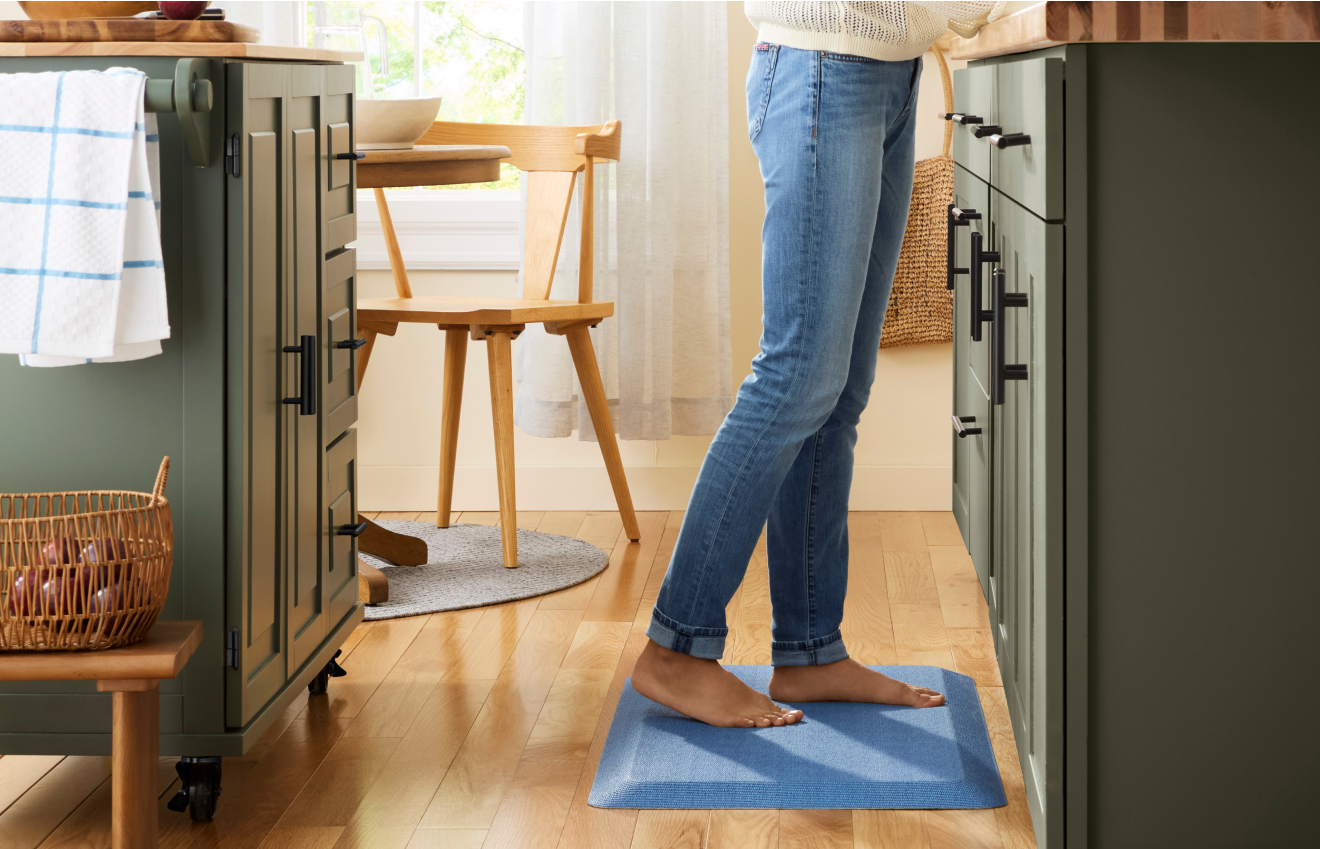 Person at a kitchen counter standing on a KitchenAid® Comfort Mat.