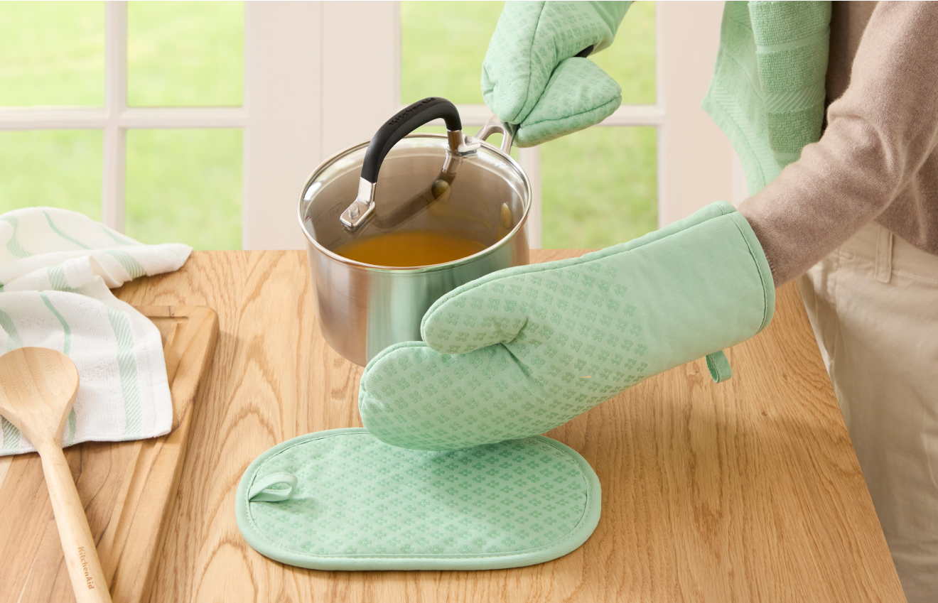 Person using KitchenAid® Oven Mitts to set sauce pan on counter.