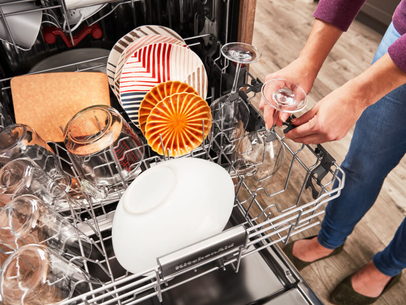 Person loading wine glasses in the top rack of a dishwasher Person loading wine glasses in the top rack of a dishwasher