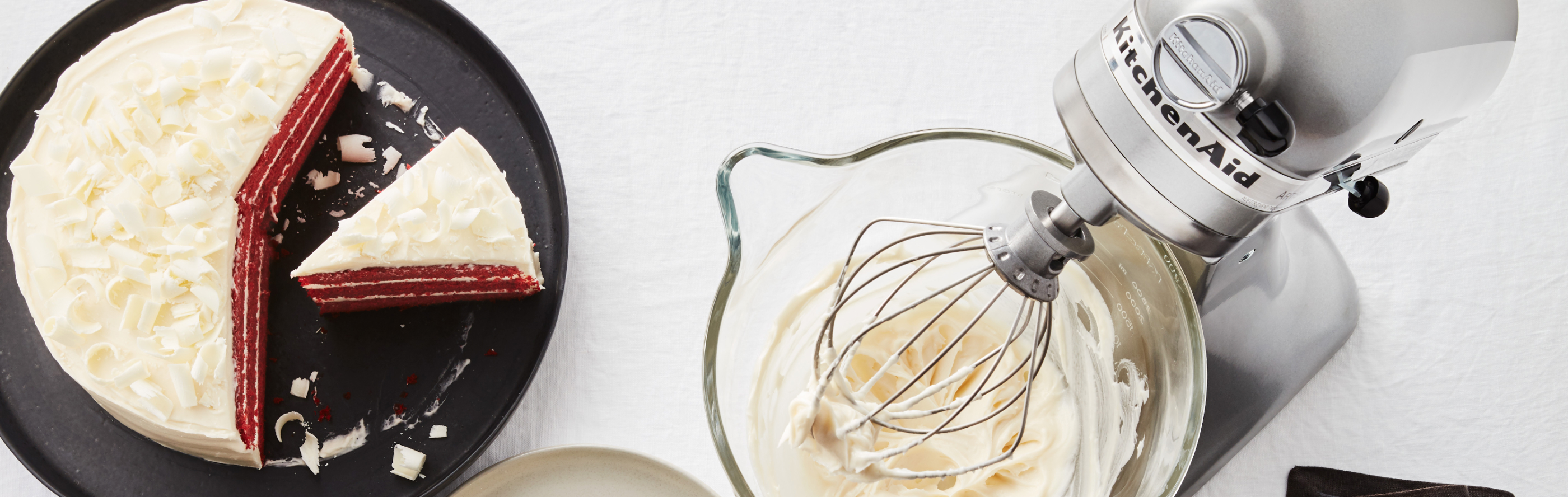 Red velvet cake next to stand mixer with frosting 