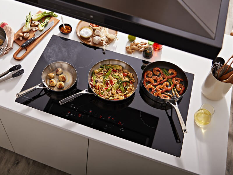 Three pans with food in them cooking on an induction cooktop