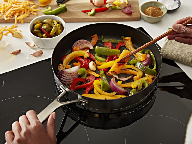 Person stirring vegetables in a pan on a cooktop