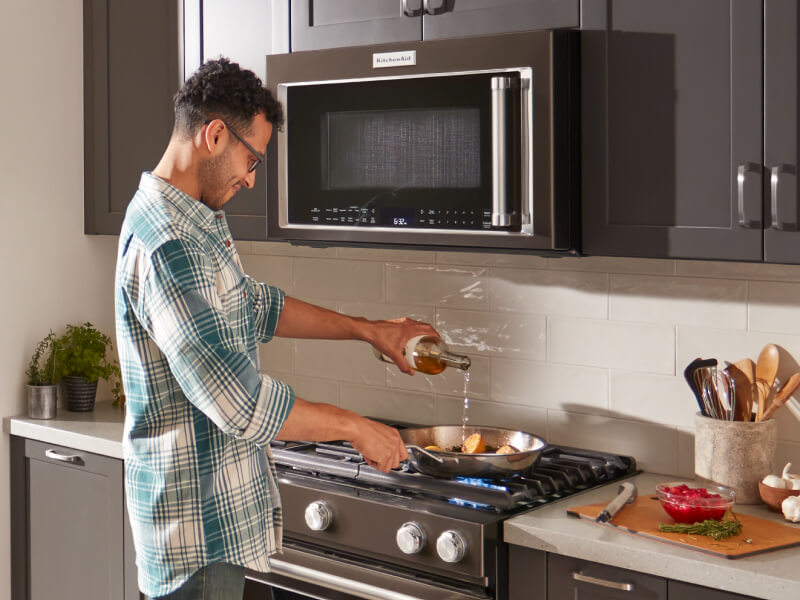 Person cooking on a stovetop with a KitchenAid® over-the-range microwave above Person cooking on a stovetop with a KitchenAid® over-the-range microwave above