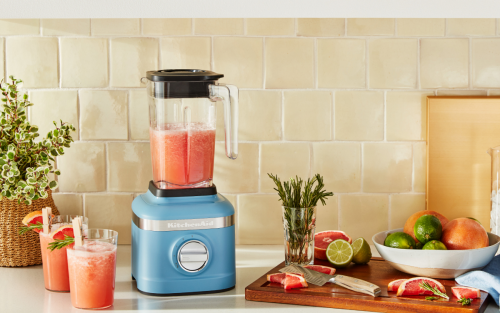 Blue blender next to two pink frosted cocktail drinks and a cutting board of ingredients