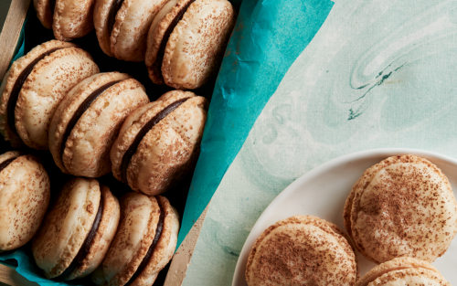 Almond macarons with dark chocolate ganache filling on a plate.