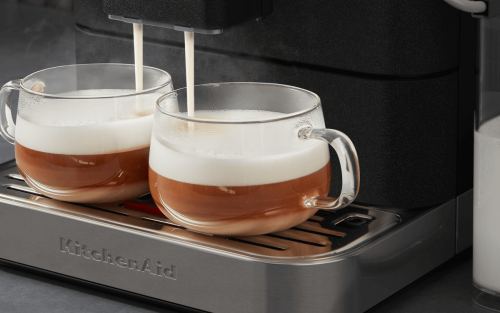 Glass mugs beneath an espresso machine being filled with frothed milk