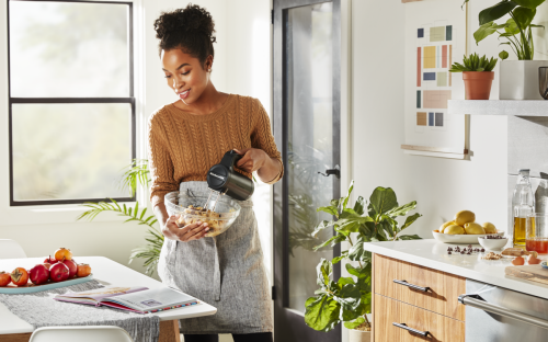 Woman holding bowl of cookie dough and mixing with cordless hand mixer.