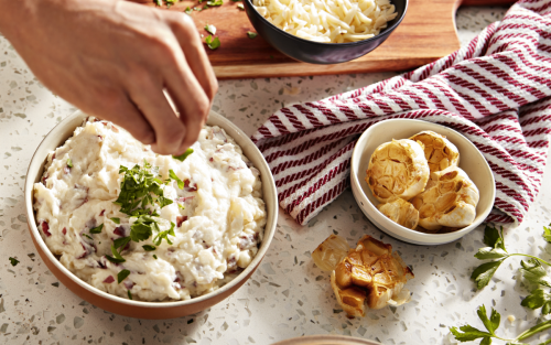 Roasted garlic beside a bowl of mashed red potatoes