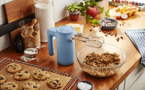 Blue KitchenAid® hand mixer on countertop next to bowl of chocolate chip cookie dough