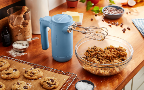 Cordless KitchenAid® hand mixer next to cookie dough and fresh baked chocolate chip cookies.