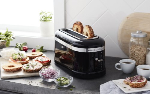 Bagel slices in a pop-up KitchenAid® toaster on a modern kitchen counter next to bagel sandwich fixings.