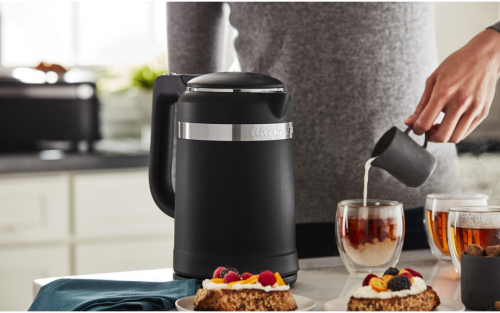 A woman pouring cream into tea next to a KitchenAid® electric kettle