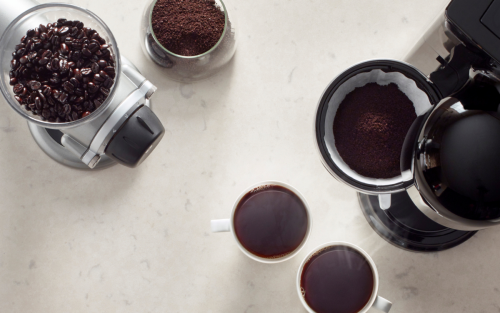 Bird’s-eye view of full cups of coffee, a coffee maker and a coffee grinder near coffee beans