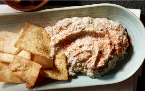 Close-up of baba ganoush garnished with paprika next to pita chips