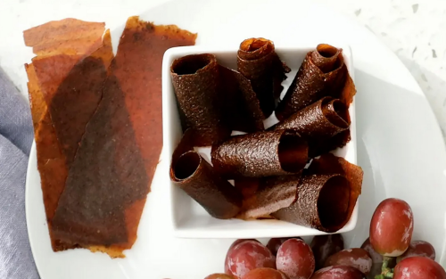 Homemade fruit leather and grapes on white dishware.