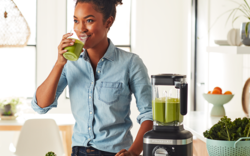 Person drinking green juice next to a KitchenAid® blender