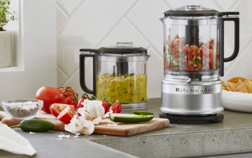 A KitchenAid® food processor and food chopper with freshly made salsa and guacamole on a modern kitchen counter.