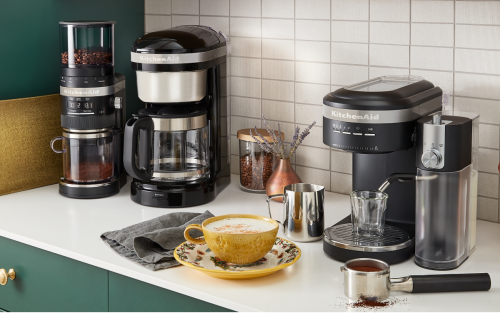 Latte in a yellow cup on white countertop next to KitchenAid® espresso machine