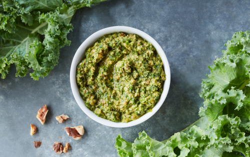 Fresh pesto in a white bowl next to kale