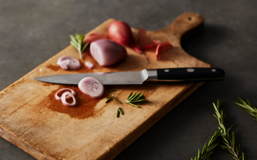 Wooden cutting board with partially cut red onion and knife on top