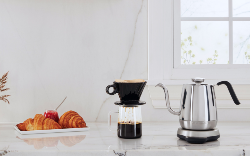 Silver KitchenAid® electric kettle on countertop with coffee and plate of croissants