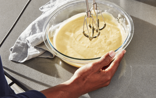 Person using hand mixer to mix white queso in glass bowl