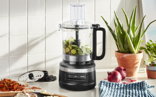  Sliced cucumbers in a KitchenAid® food processor next to shredded vegetables