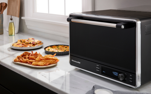 A KitchenAid® countertop oven with air fry on a modern kitchen counter next to air fried appetizers.