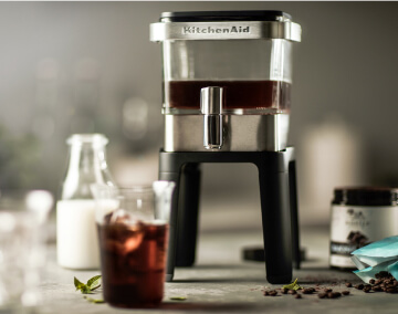 KitchenAid® Cold Brew Coffee Maker with bottle of cream, and glass of iced coffee in foreground.