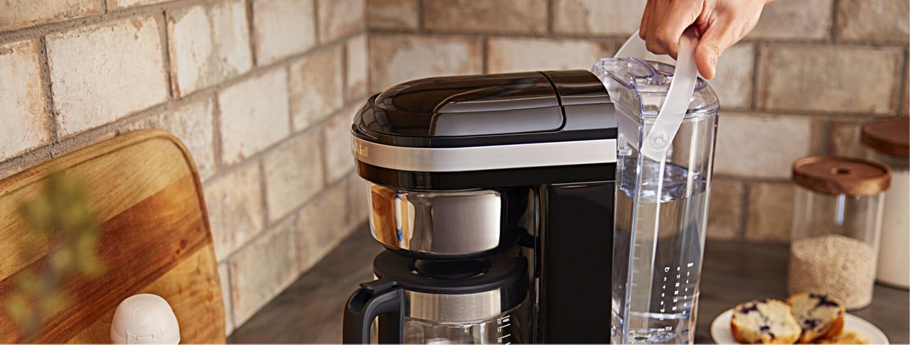 Hand removing water reservoir from base of KitchenAid® Drip Coffee maker.