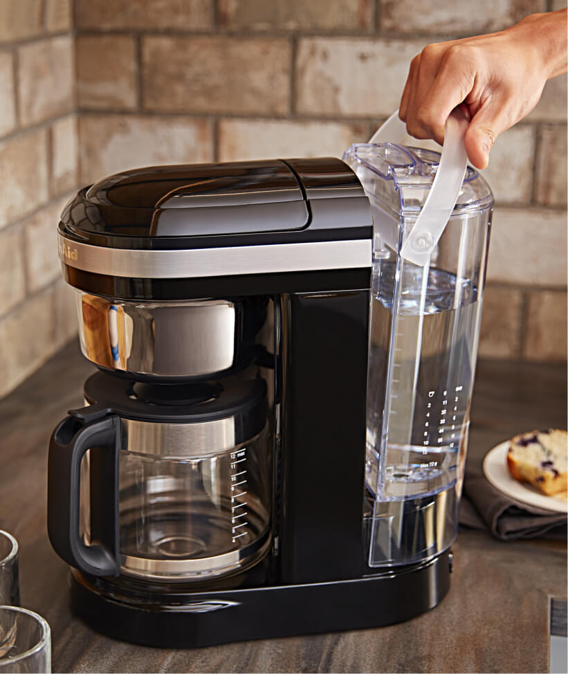 Hand removing water reservoir from base of KitchenAid® Drip Coffee maker.