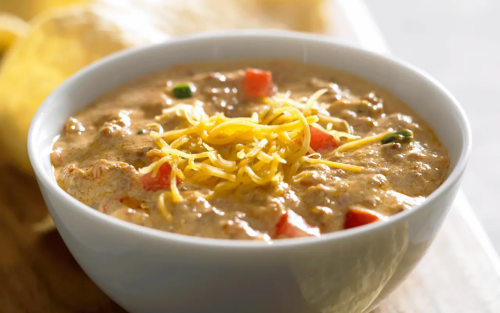 A bowl of homemade queso with shredded cheese sprinkled on top.