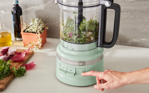 Close-up of mint green food processor shredding mixed greens