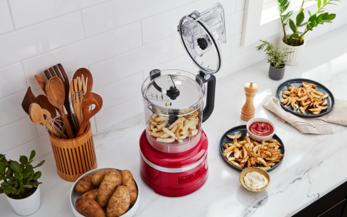 A countertop of plated potato dishes and potatoes in a food processor