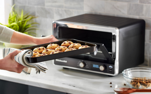 A person pulling freshly baked chocolate chip cookies out of a countertop oven