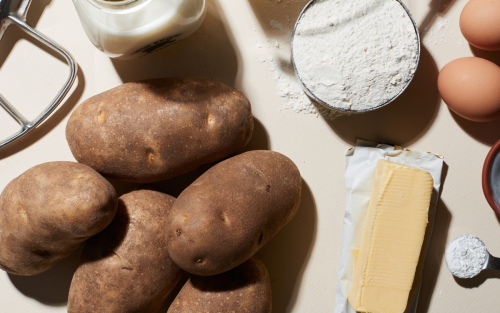 Russet potatoes on white countertop with assorted ingredients