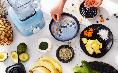 Person garnishing a blue smoothie bowl next to blue KitchenAid® blender