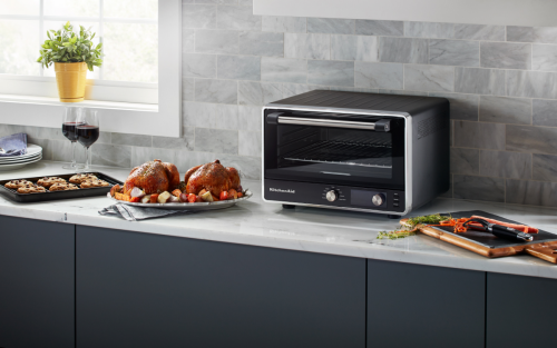 KitchenAid® countertop oven next to roasted chicken and a tray of cookies