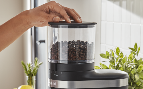 A woman preparing to process coffee beans in a black coffee grinder