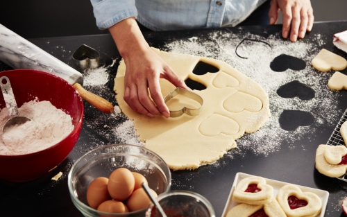 A piece of dough being pressed with a cookie cutter, surrounded by other baking instruments