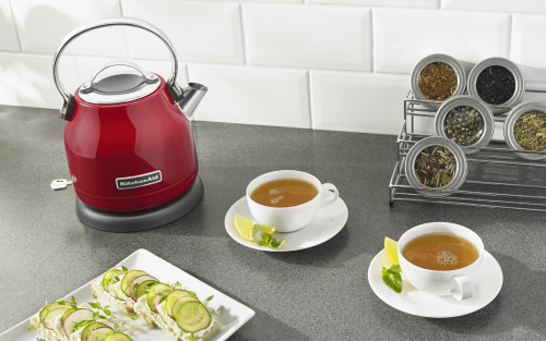 KitchenAid® electric tea kettle on countertop with cups of tea and containers of loose tea leaves.