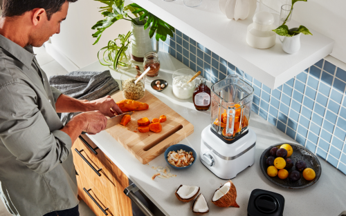 A man in a modern kitchen cutting vegetables to add to a KitchenAid® blender. 