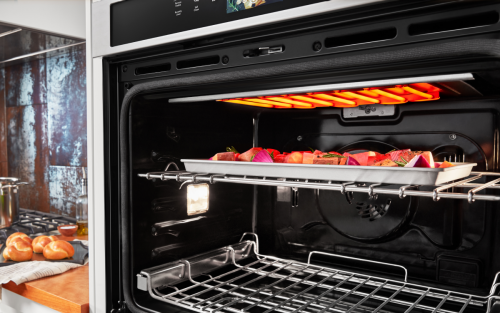 Assorted vegetables on a sheet pan broiling in an open wall oven