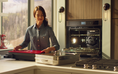 A woman placing a red baking stone into a wall oven