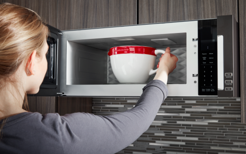 A woman placing a bowl in a KitchenAid® microwave.