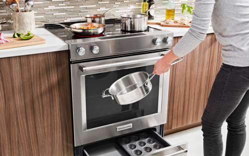 A person holding a pot in front of a KitchenAid® slide-in range