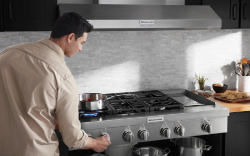 A man turning up a burner to cook food on a stainless steel rangetop